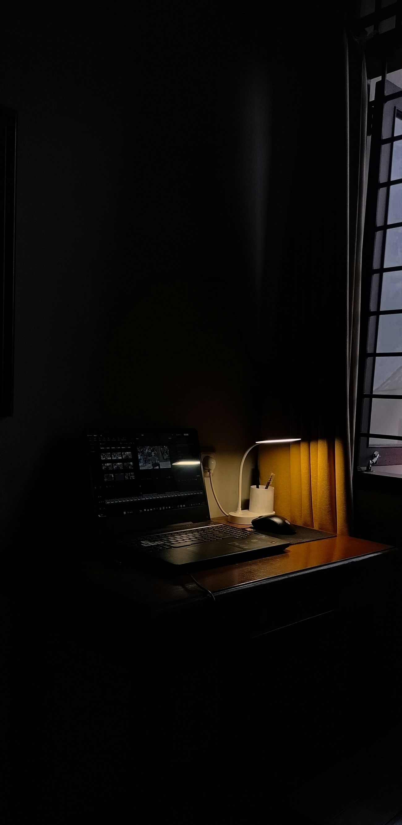 Notebook sobre uma mesa à noite iluminado por uma única luminária, presença que brilha no escuro